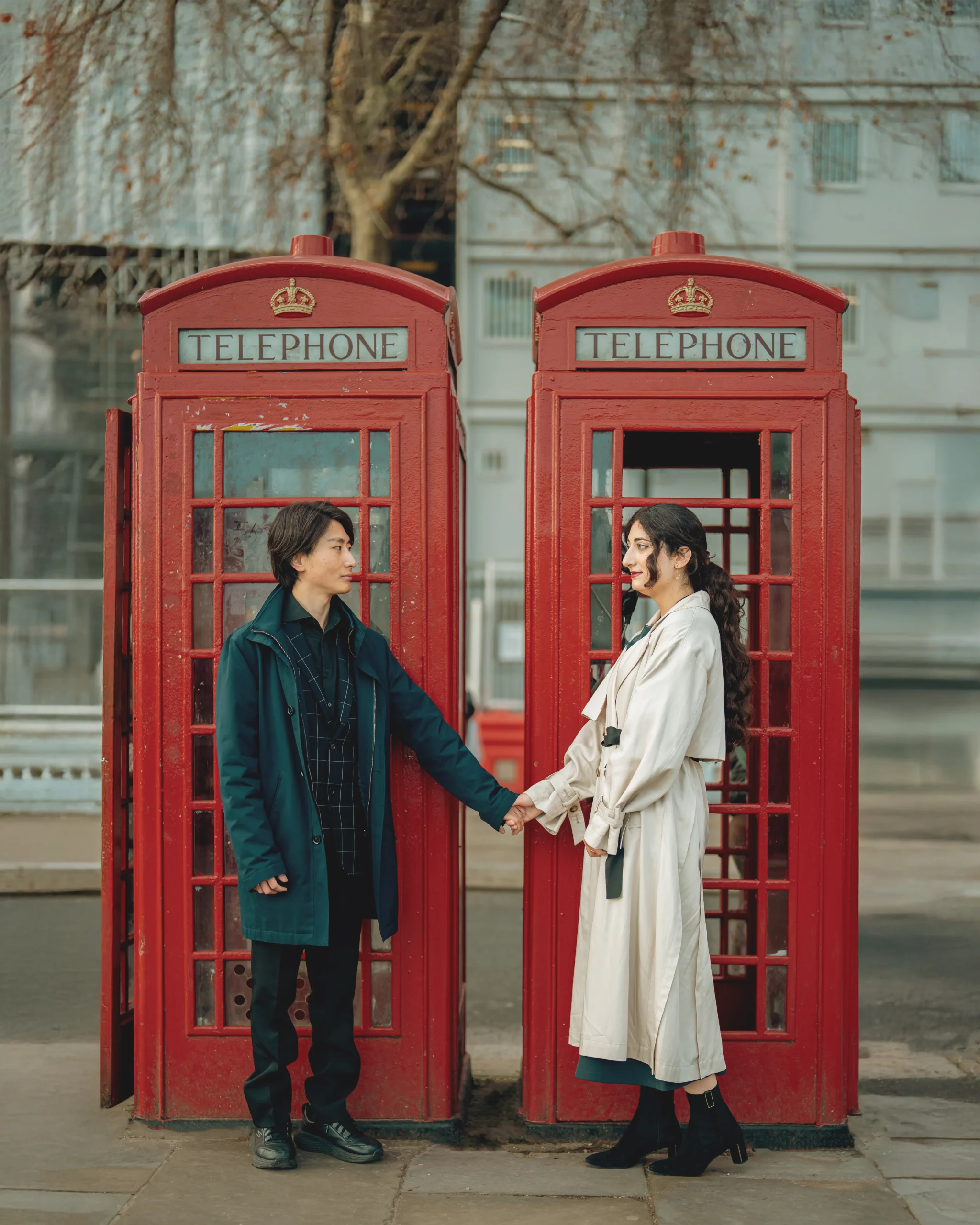 A romantic couple holding hands between two iconic red telephone booths in London, captured by London Snap photography agency.